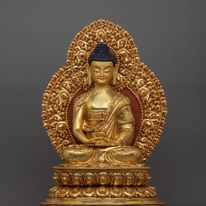 K&ouml;nnte beinhalten: Eine goldfarbene Buddha-Statue, die in meditativer Haltung sitzt. Die Statue ist mit aufwendigen Details verziert und auf einem lotusf&ouml;rmigen Sockel platziert.