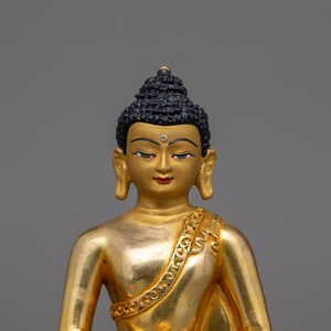 May include: A gold-colored statue of Buddha, with a black hair and a serene expression. The statue is sitting in a meditative pose.