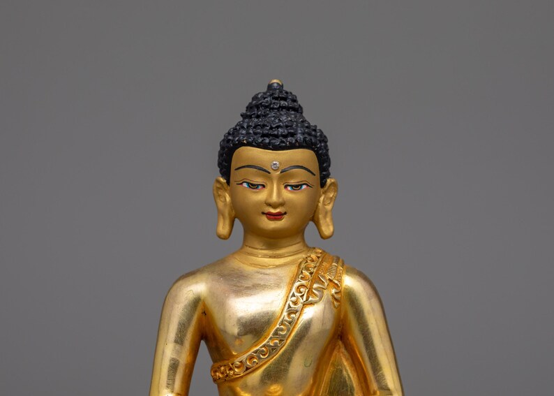 May include: A gold-colored statue of Buddha, with a black hair and a serene expression. The statue is sitting in a meditative pose.