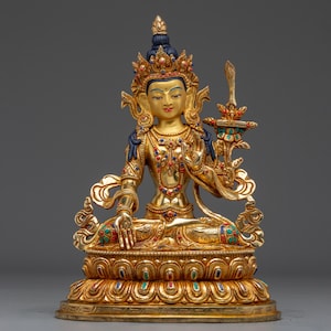 Puede incluir: Una estatua dorada de una deidad sentada con detalles intrincados. La figura lleva una corona y joyas, sosteniendo un objeto ornamentado. La estatua está adornada con detalles rojos, azules y verdes, y se asienta sobre una base detallada.