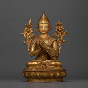 Puede incluir: Una estatua dorada de una figura sentada con una corona y las manos en posición de oración. La figura está rodeada de motivos florales.