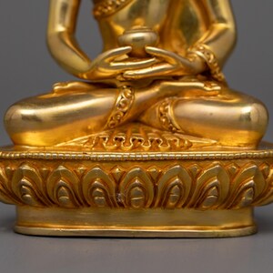 May include: A gold-colored statue of a seated Buddha with a lotus base. The Buddha is holding a small bowl in their hands.