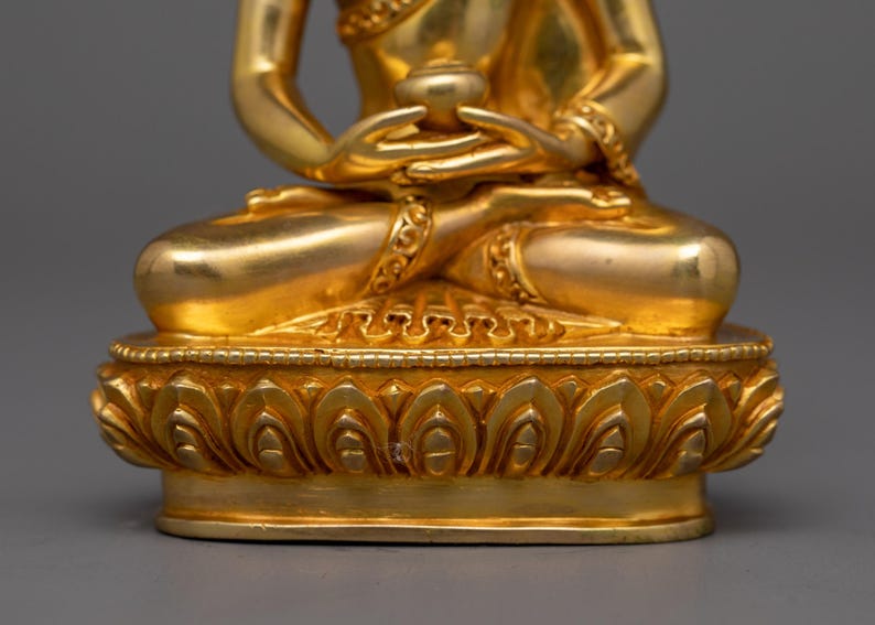 May include: A gold-colored statue of a seated Buddha with a lotus base. The Buddha is holding a small bowl in their hands.