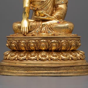 K&ouml;nnte beinhalten: Eine goldfarbene Statue eines Buddha, der in Meditation auf einem Lotussockel sitzt. Die Statue ist aufwendig verziert und hat einen ruhigen Ausdruck.