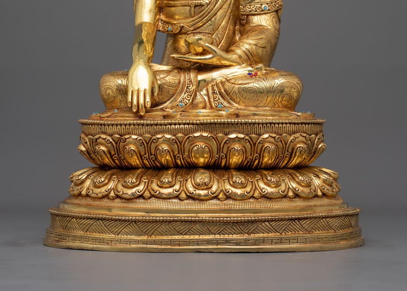 K&ouml;nnte beinhalten: Eine goldfarbene Statue eines Buddha, der in Meditation auf einem Lotussockel sitzt. Die Statue ist aufwendig verziert und hat einen ruhigen Ausdruck.