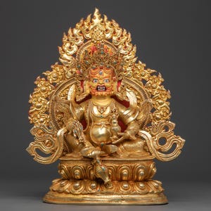 Könnte beinhalten: Eine goldene Statue einer Gottheit, sitzend auf einem Lotus-Sockel, mit aufwendigen Details. Die Figur hat einen grimmigen Ausdruck, geschmückt mit einer Krone und Schmuck. Der Hintergrund weist verzierte, flammenartige Muster auf. Die Statue ist wahrscheinlich aus Metall und ein religiöses oder dekoratives Objekt.
