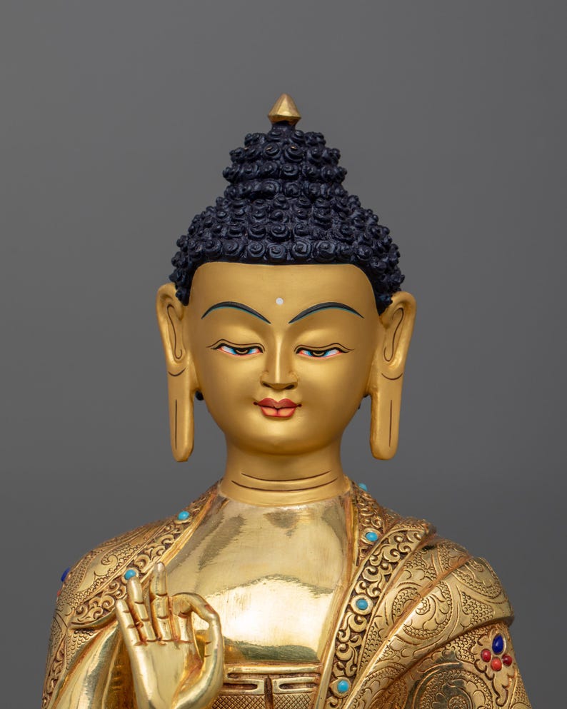 K&ouml;nnte beinhalten: Eine goldene Buddha-Statue mit einem detaillierten, verzierten Gewand und einem ruhigen Ausdruck. Die Statue ist aus Metall und hat ein traditionelles Design.