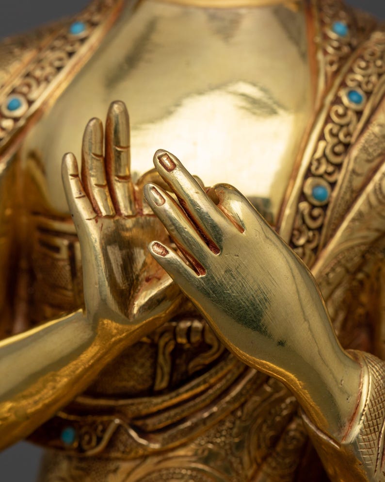 K&ouml;nnte beinhalten: Nahaufnahme der H&auml;nde einer goldenen Statue in Gebetsposition. Die H&auml;nde sind mit aufwendigen Schnitzereien verziert und mit t&uuml;rkisfarbenen Edelsteinen besetzt.