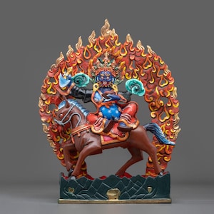 Könnte beinhalten: Eine mehrfarbige Statue einer blauhäutigen Gottheit auf einem braunen Pferd vor einem großen, verzierten, flammenförmigen Hintergrund. Die Figur trägt eine Krone und bunte Gewänder, hält ein blaues Objekt und steht auf einem dunkelgrünen Sockel.