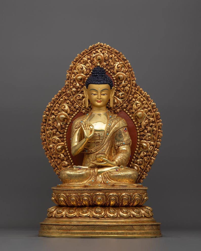 K&ouml;nnte beinhalten: Eine goldfarbene Buddha-Statue, die in meditativer Haltung sitzt. Die Statue ist mit aufwendigen Details verziert und vor einem grauen Hintergrund platziert.