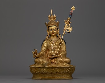 May include: A gold-colored statue of a seated figure with a crown and a scepter. The figure is wearing elaborate clothing and jewelry. The statue is on a base with a lotus design.