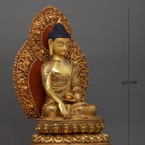 K&ouml;nnte beinhalten: Eine goldfarbene Buddha-Statue, die in meditativer Haltung sitzt und einen Heiligenschein hinter dem Kopf hat. Die Statue ist 45 cm hoch und 29 cm breit.