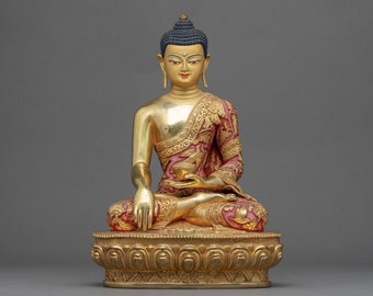 May include: A gold-painted statue of Buddha sitting in meditation with a red and gold robe. The statue is on a gold base with intricate details.