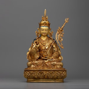 May include: A gold-colored statue of a seated figure with a crown and a scepter. The figure is wearing a robe with intricate details and has a serene expression.