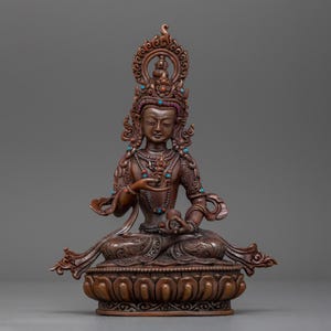 May include: An ornate brown statue of a deity seated in a meditative pose. The statue is decorated with turquoise and red gemstones. The deity is wearing a crown and has a serene expression.