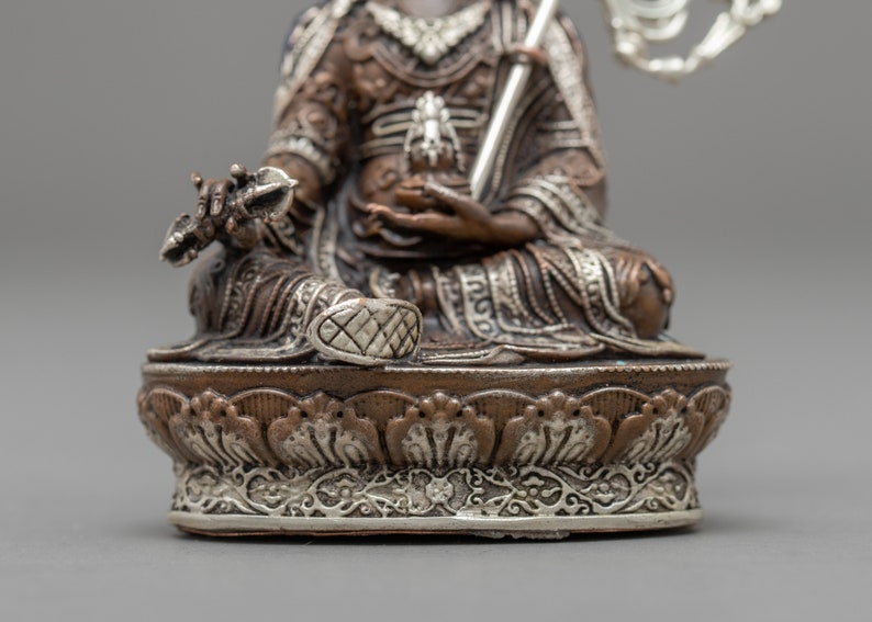 May include: A silver and copper colored statue of a seated figure with a crown and a scepter. The statue is intricately detailed and has a decorative base.