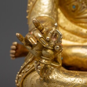 K&ouml;nnte beinhalten: Nahaufnahme einer goldenen Statue, die komplizierte Details zeigt. Die Hand der Statue h&auml;lt ein detailliertes, verziertes Objekt. Die Figur ist mit aufwendigen Mustern und Designs geschm&uuml;ckt, wobei der Fokus auf der Hand und dem Objekt liegt.