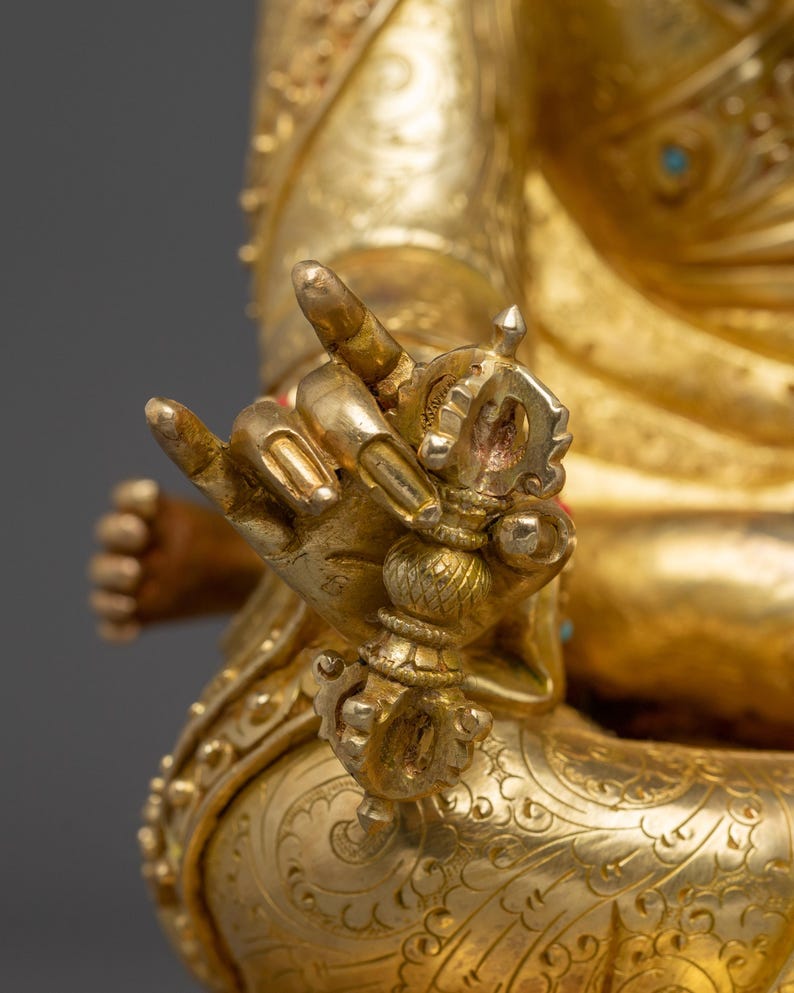 K&ouml;nnte beinhalten: Nahaufnahme einer goldenen Statue, die komplizierte Details zeigt. Die Hand der Statue h&auml;lt ein detailliertes, verziertes Objekt. Die Figur ist mit aufwendigen Mustern und Designs geschm&uuml;ckt, wobei der Fokus auf der Hand und dem Objekt liegt.