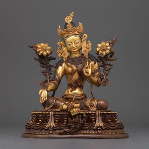 Könnte beinhalten: Eine goldene und schwarze Statue einer sitzenden weiblichen Gottheit mit einer Krone und Blumen. Die Statue steht auf einem Sockel mit aufwendigen Schnitzereien.