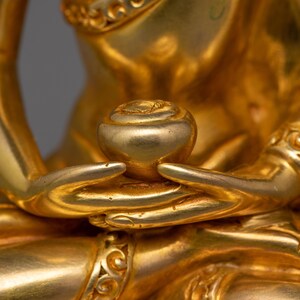 May include: Close-up of a golden statue's hands holding a small, round, golden object. The statue is intricately detailed with ornate patterns.