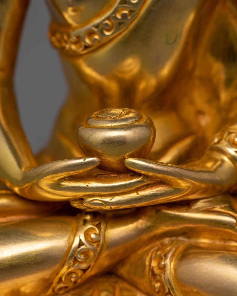 May include: Close-up of a golden statue's hands holding a small, round, golden object. The statue is intricately detailed with ornate patterns.