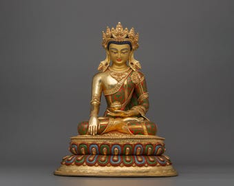 May include: A gold-painted statue of a seated Buddha with a green and red robe, a crown, and a lotus flower in its hand. The statue is on a multi-colored base with gold accents.