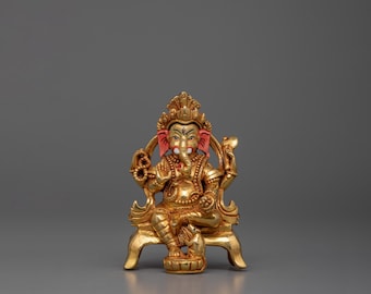 May include: A gold-colored statue of Ganesha, the Hindu god of wisdom and prosperity, sitting on a throne. The statue is intricately detailed and features red accents on the ears and a white trunk.