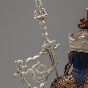 May include: Close-up of a silver and gold statue with a detailed design. The statue has a crown and a silver scepter with a decorative top.