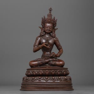 Puede incluir: Una estatua de bronce de un Buda sentado con una corona y detalles intrincados. La estatua está sobre una base escalonada con un diseño de loto.