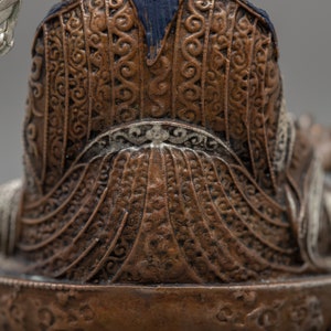 May include: A detailed bronze statue of a seated figure with intricate patterns on the clothing. The figure is wearing a blue robe with a silver crown and holding a staff.