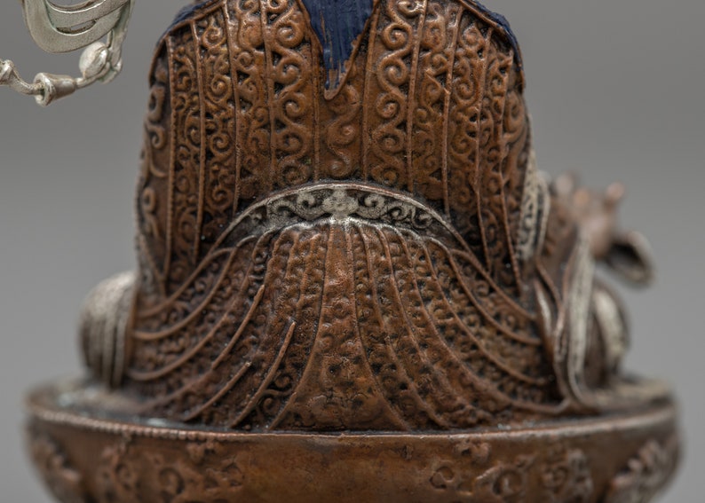 May include: A detailed bronze statue of a seated figure with intricate patterns on the clothing. The figure is wearing a blue robe with a silver crown and holding a staff.
