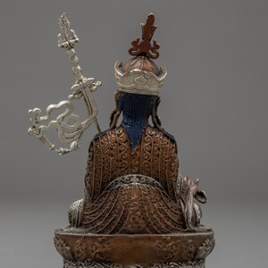May include: A copper and silver Tibetan Buddhist statue of a seated figure with a crown and ornate clothing. The figure holds a silver scepter in their right hand.