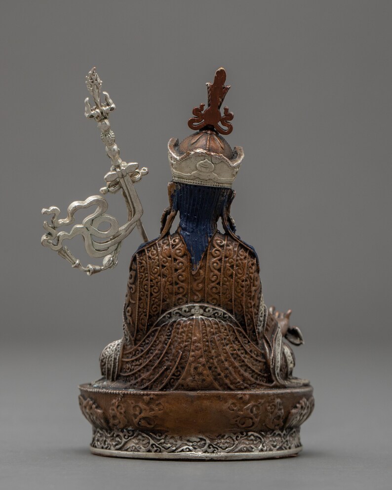 May include: A copper and silver Tibetan Buddhist statue of a seated figure with a crown and ornate clothing. The figure holds a silver scepter in their right hand.