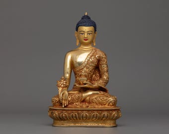 May include: A gold-coloured Buddha statue with a detailed, ornate design. The statue is sitting in a meditative pose with hands in the mudra position. The Buddha has a serene expression and is wearing a traditional robe.