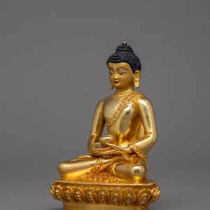 May include: A gold-colored Buddha statue sitting in a meditative pose with hands in the Dhyana mudra. The statue is detailed with intricate carvings and is set on a lotus base.