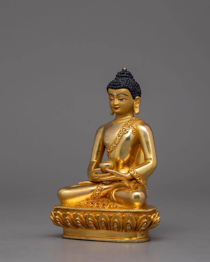 May include: A gold-colored Buddha statue sitting in a meditative pose with hands in the Dhyana mudra. The statue is detailed with intricate carvings and is set on a lotus base.