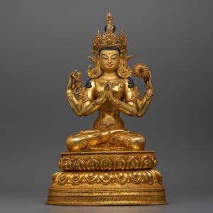 May include: A gold-coloured statue of a four-armed deity sitting in a meditative pose. The deity is adorned with intricate jewellery and a crown. The statue is set on a multi-tiered base.