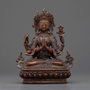 Puede incluir: Una estatua de bronce de cuatro brazos de una deidad con una corona y una flor en una mano. La estatua está sentada en una postura meditativa con las manos en posición de oración. La estatua está sobre una base de loto.