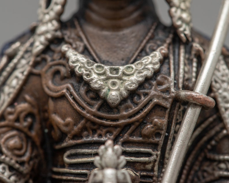 May include: Close-up of a bronze statue of a warrior wearing ornate armor with silver accents. The warrior is holding a spear in their right hand.