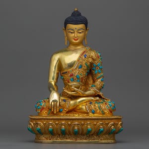 Peut inclure: Une statue dorée de Bouddha avec des accents turquoise et rouges est assise en position méditative sur une base dorée aux détails complexes.