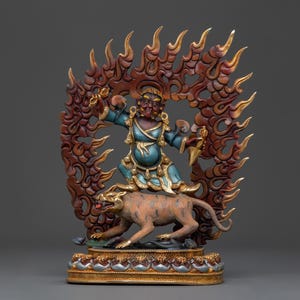 May include: A detailed statue of a deity with a fierce expression, clad in blue and gold robes, standing atop a tiger. The figure is surrounded by a carved wooden frame with flame-like details. The base is ornate with gold accents.