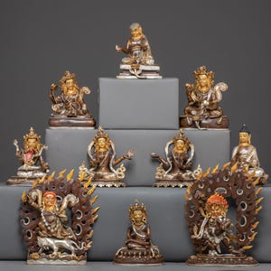 May include: A collection of ornate, gold-toned statues of various sizes and poses, arranged on gray platforms. The statues depict figures with detailed features, some with halos or elaborate backdrops. The overall aesthetic is one of religious or spiritual art.