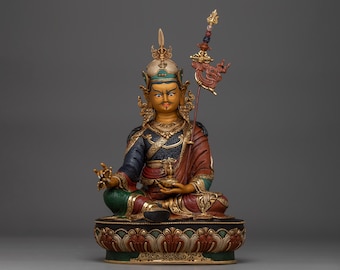 May include: A seated, ornate statue of a figure in a meditative pose. The figure wears a detailed headdress, blue and red robes, and holds a staff. The statue is on a decorative base with gold accents.