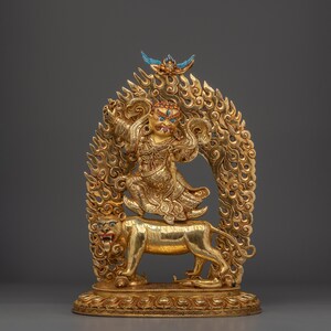 May include: A golden statue depicting a deity riding a lion, set against a fiery backdrop. The deity has a fierce expression, adorned with colorful accents. The statue is intricately detailed, showcasing a blend of religious and artistic elements.