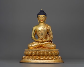 May include: A gold-colored statue of Buddha sitting in meditation pose. The statue is detailed with intricate carvings and is set on a multi-tiered base.