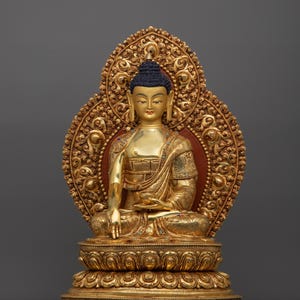 K&ouml;nnte beinhalten: Eine goldfarbene Buddha-Statue, die in meditativer Haltung sitzt. Die Statue ist mit aufwendigen Details verziert und vor einem grauen Hintergrund platziert.