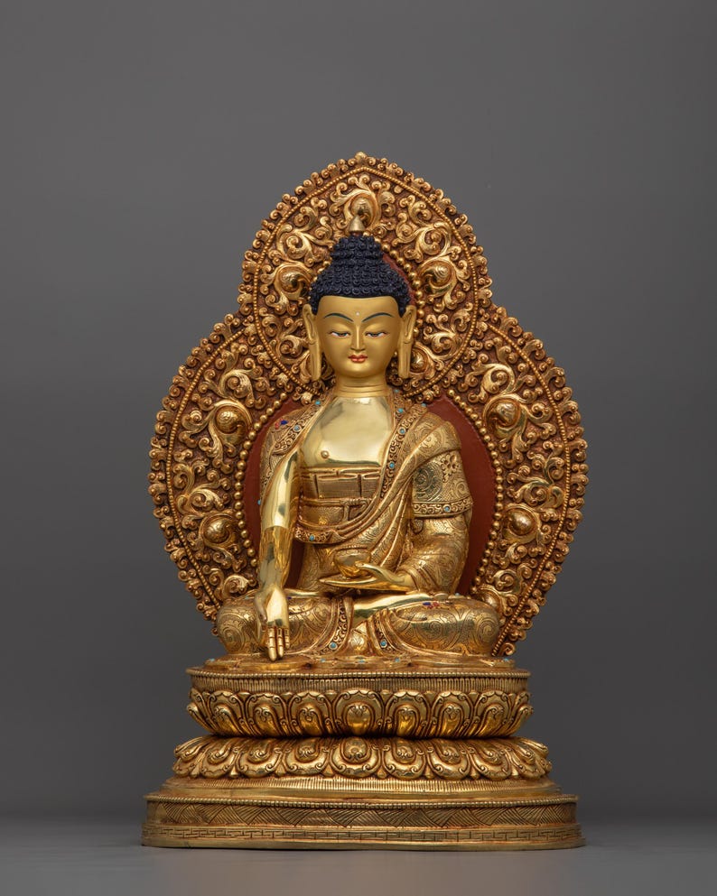 K&ouml;nnte beinhalten: Eine goldfarbene Buddha-Statue, die in meditativer Haltung sitzt. Die Statue ist mit aufwendigen Details verziert und vor einem grauen Hintergrund platziert.