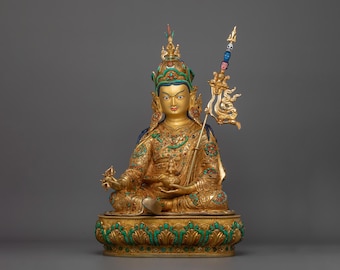 May include: A gold-colored statue of a deity, sitting in a meditative pose. The statue is adorned with intricate details, including a crown, jewelry, and a scepter. The deity is seated on a lotus throne with a green and gold base.