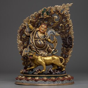 May include: A detailed, gold-colored statue of a deity riding a golden tiger. The deity is depicted with a fierce expression, holding a weapon, and is surrounded by ornate, swirling patterns. The base is multi-colored.