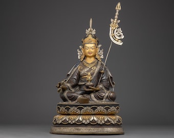 May include: A detailed statue of a seated figure with a gold face and ornate headdress. The figure wears a dark robe and holds a small object. A decorative staff with a silver and gold design is held in the right hand. The statue sits on a detailed base.